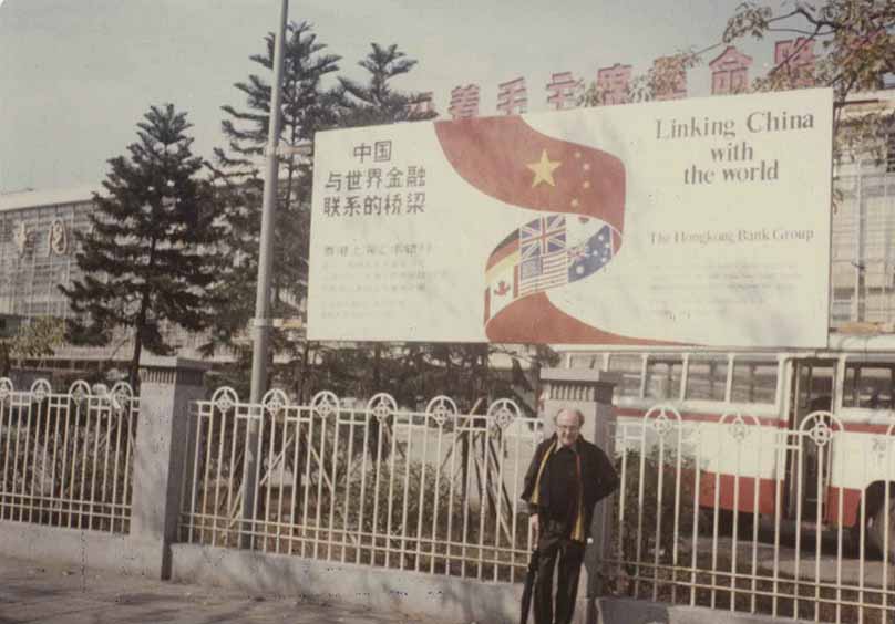 Photograph taken in Shanghai in 1983 showing retired  employee Brian Ogden standing by an advert for HSBC. The advert reads &#039;Linking China with the World&#039;